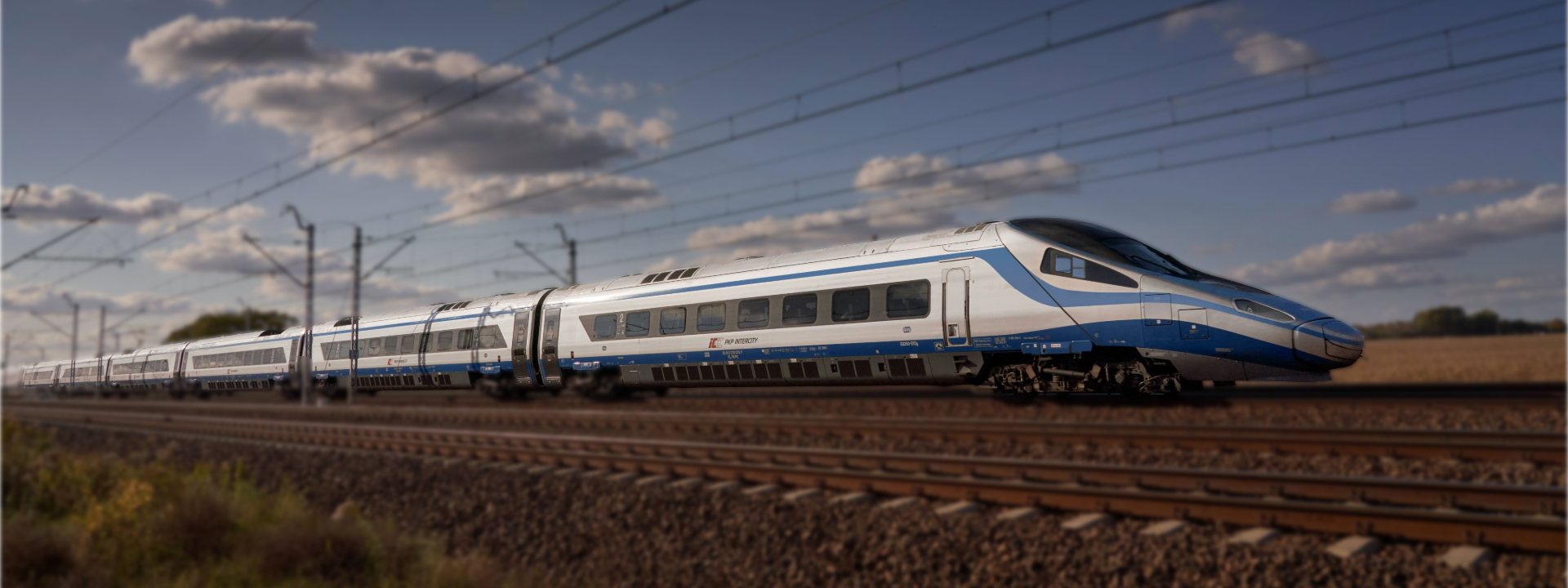 Ein weiß-blauer PKP Intercity Pendolino Hochgeschwindigkeitszug fährt auf Bahngleisen durch eine ländliche Gegend in Polen. 