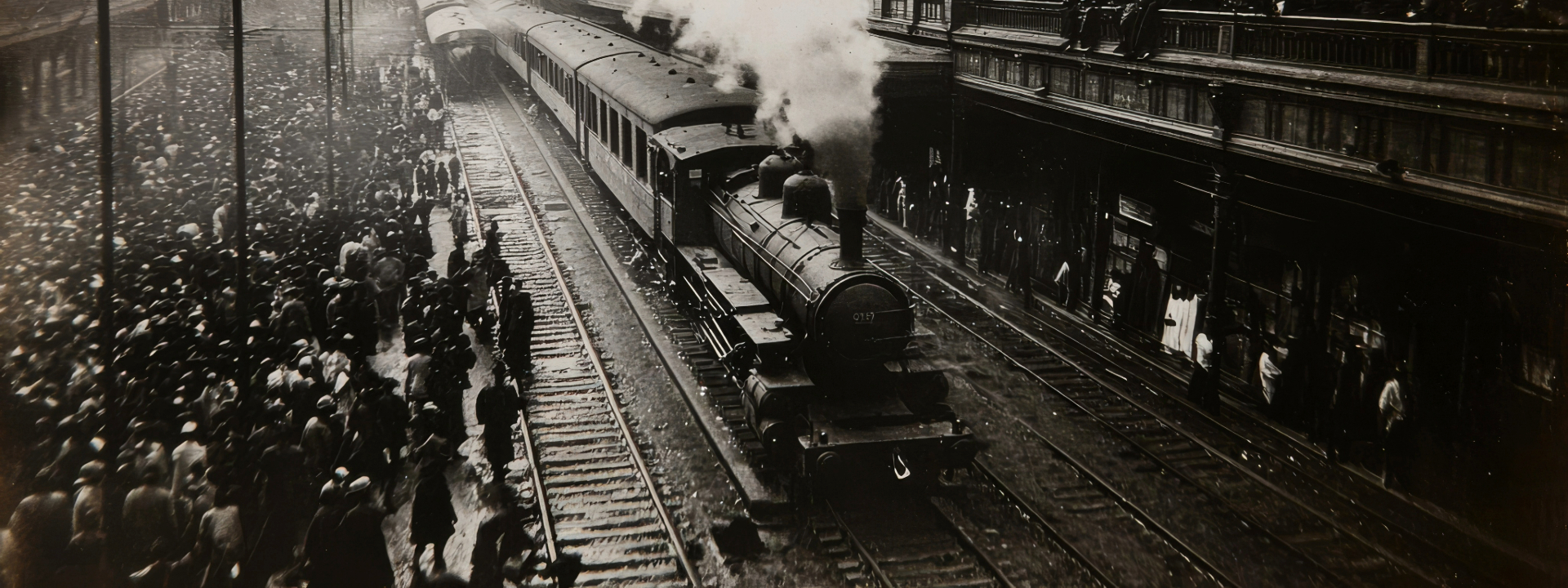 Historische Schwarz-Weiß-Fotografie (Sepia-Ton) einer alten Dampflokomotive mit Waggons an einem vollen Bahnsteig mit vielen wartenden Menschen aus der Vogelperspektive.