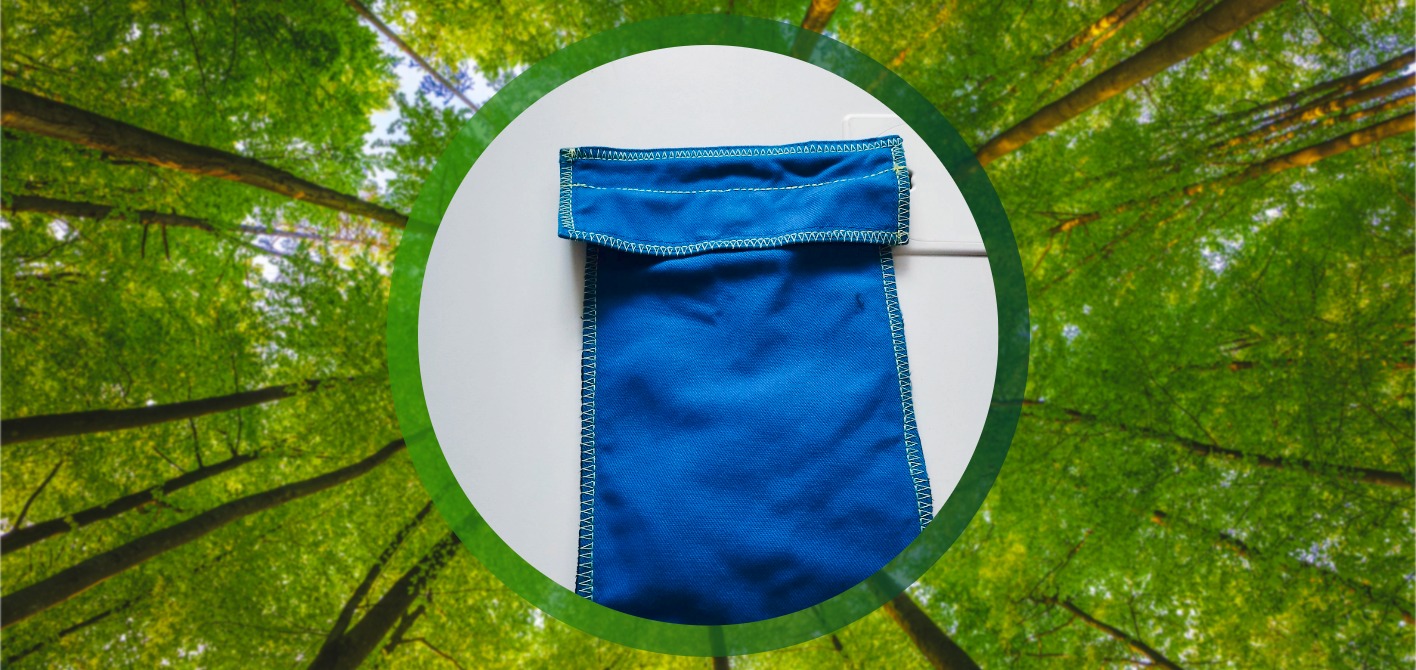 Upcycling und Ressourcenschonung: Aus alter Dienstkleidung wird Gutes Eine rechteckige, dunkelblaue Tasche aus Stoff mit gelber Naht liegt auf einem weißen Hintergrund. Die Szene, umrahmt von grünen Baumkronen, stellt das Upcycling von Materialien für die Nachhaltigkeit dar.