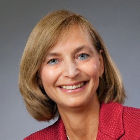 Nahaufnahme Porträt von Britta Mas, Fachbereichsleiterin Nachhaltigkeit beim VDV, mit einem freundlichen Lächeln vor einem grauen Hintergrund.