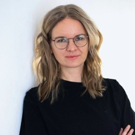 Nahaufnahme Porträt von Mareike Rehl, Fachbereichsleiterin Nachhaltigkeit bei der VAG, die eine Brille trägt und sich an eine weiße Wand lehnt.