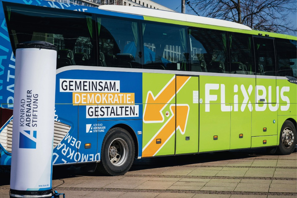 Luftaufnahme einer Gleisbaustelle im herbstlichen Wald: Ein grüner Schienenkran hebt ein großes, gewölbtes Betonelement vor ein Tunnelportal der Hermann-Hesse-Bahn, um eine Einhausung für den Fledermausschutz zu errichten
