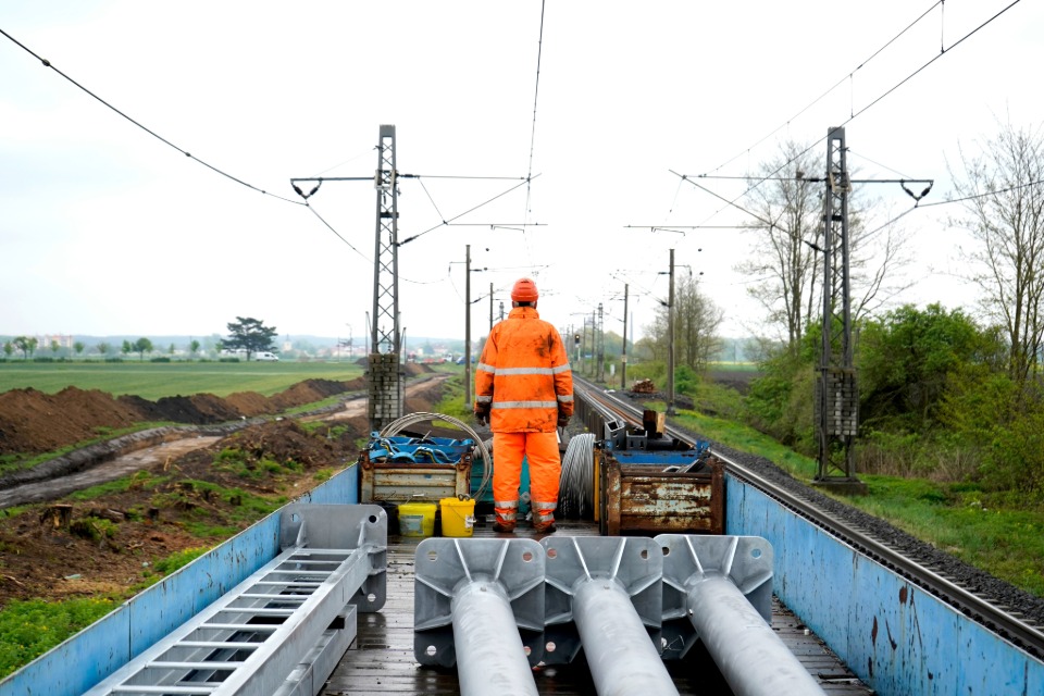 Luftaufnahme einer Gleisbaustelle im herbstlichen Wald: Ein grüner Schienenkran hebt ein großes, gewölbtes Betonelement vor ein Tunnelportal der Hermann-Hesse-Bahn, um eine Einhausung für den Fledermausschutz zu errichten
